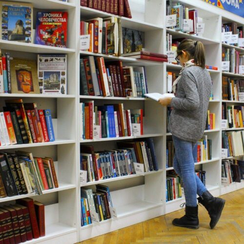 Frau sucht in einem Bücherregal einer Bibliothek nach einem Buch
