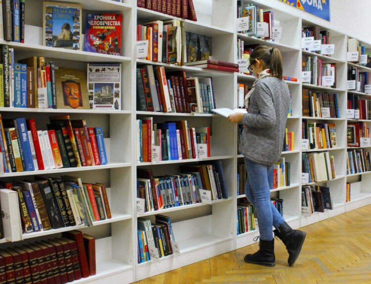 Frau sucht in einem Bücherregal einer Bibliothek nach einem Buch